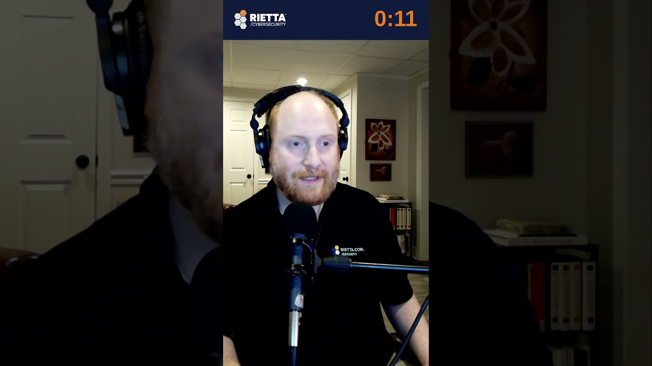Frank Rietta in a Rietta Cybersecurity shirt and headphones, speaking into a studio microphone in his office, under a Rietta Cybersecurity title bar.
