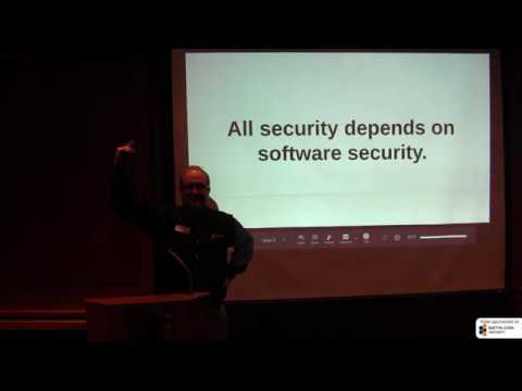 Frank Rietta presenting on a dark stage at a podium, with a projected slide reading "All security depends on software security."